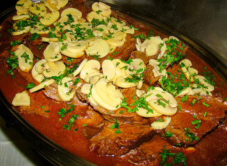 A tray with fillet mignon steaks in Madeira sauce, topped with slices of champignon, Paris mushrooms and green scented pepper, sprinkled on top.