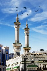 a bird flying in front of a building with a blue sky in the background The minarets of the Mecca