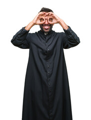 Adult hispanic catholic priest man over isolated background doing ok gesture like binoculars sticking tongue out, eyes looking through fingers. Crazy expression.