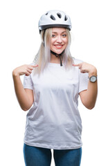 Young blonde woman wearing cyclist security helmet over isolated background looking confident with smile on face, pointing oneself with fingers proud and happy.