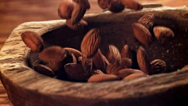Almonds, a natural ingredient, are cascading onto a wooden table. This closeup, macro photography showcases the nuts in their shell, portraying a still life of natural foods