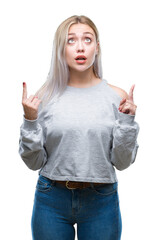 Young blonde woman over isolated background amazed and surprised looking up and pointing with fingers and raised arms.