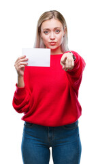 Young blonde woman holding blank paper card over isolated background pointing with finger to the camera and to you, hand sign, positive and confident gesture from the front