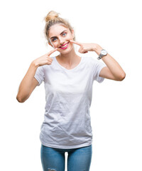 Young beautiful blonde woman wearing white t-shirt over isolated background smiling confident showing and pointing with fingers teeth and mouth. Health concept.