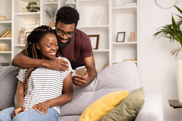 Happy Couple Relaxing On Sofa At Home With Smartphone, Casual Lifestyle, Modern Living Room Interior - obrazy, fototapety, plakaty