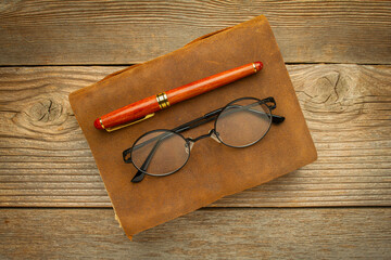 antique leatherbound journal with stylish pen and reading glasses on a rustic wooden table, journaling concept