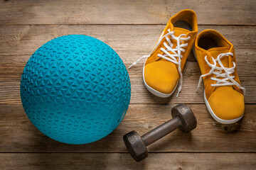 heavy rubber slam ball filled with sand, iron dumbbell and minimalist barefoot sneakers on a rustic wooden deck, exercise and fitness concept
