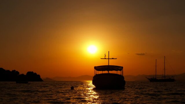 Floating touristic ship in dark sunset. A view of sunset time over the coast with anchored boat during summer time.
