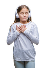 Young beautiful girl wearing headphones listening to music over isolated background smiling with hands on chest with closed eyes and grateful gesture on face. Health concept.