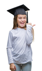 Young beautiful girl wearing graduate cap over isolated background smiling with happy face looking and pointing to the side with thumb up.