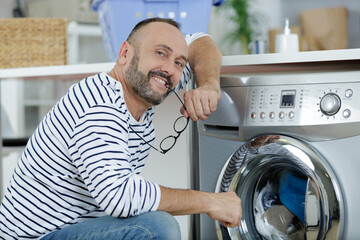 man loading clothes into washing machine - obrazy, fototapety, plakaty