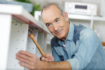 senior man hammering kitchen unit into place - 781665565