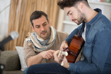 concentrated focused mature father helping student to play guitar