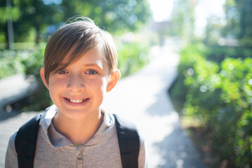 portrait of a smiling, 11 year old schoolboy with a backpack in the park