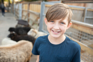 10 year old boy in front of sheep on a farm or zoo