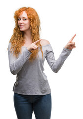 Young redhead woman smiling and looking at the camera pointing with two hands and fingers to the...