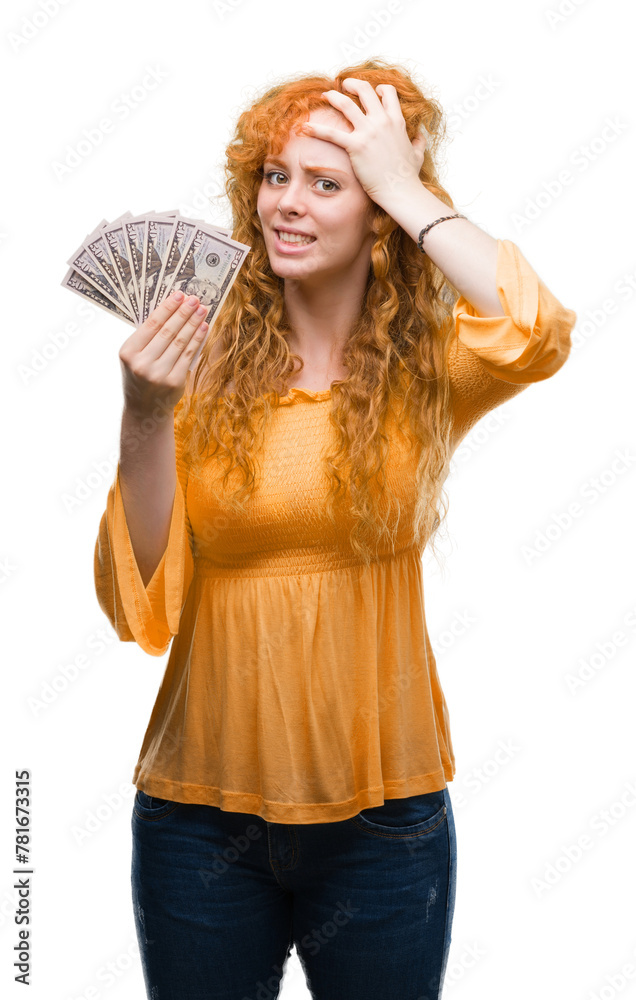 Poster Young redhead woman holding dollars stressed with hand on head, shocked with shame and surprise face, angry and frustrated. Fear and upset for mistake.