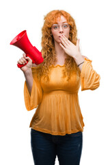 Young redhead woman holding megaphone cover mouth with hand shocked with shame for mistake, expression of fear, scared in silence, secret concept