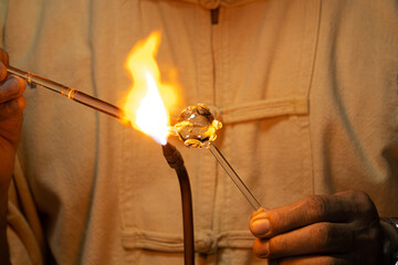 A man is holding a glass object that is being heated by a flame. Concept of craftsmanship and...