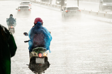 A man on a motorcycle is wearing a blue raincoat and riding in the rain. The scene is wet and...