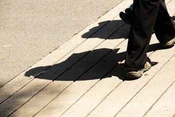 A person is walking on a sidewalk with a shadow of their foot on the ground - Powered by Adobe