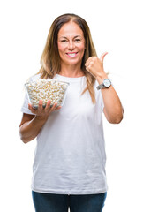 Middle age hispanic woman eating popcorn over isolated background pointing and showing with thumb...
