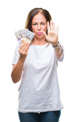 Middle age hispanic woman holding bunch of dollars over isolated background with open hand doing stop sign with serious and confident expression, defense gesture