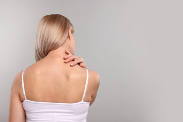 Woman suffering from pain in her neck on grey background, back view. Space for text