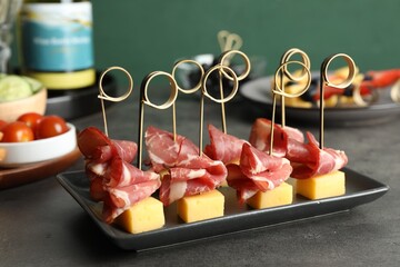 Tasty canapes with ham and cheese on grey table, closeup