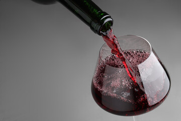 Pouring tasty red wine in glass at gray table, closeup. Space for text