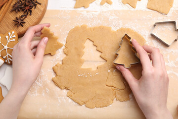 Woman making Christmas cookies with cutters at white table, top view
