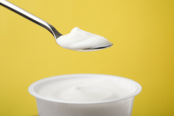 Eating delicious natural yogurt on yellow background, closeup