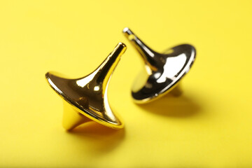 Golden and silver spinning tops on yellow background, closeup