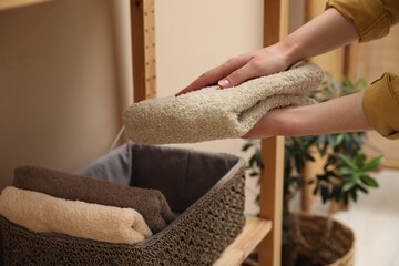 Woman putting towel into storage basket indoors, closeup