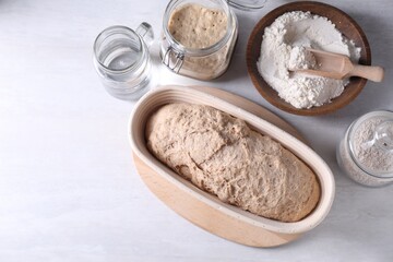 Fresh sourdough in proofing basket, flour and water on light table, flat lay. Space for text