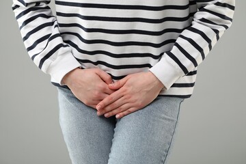 Woman suffering from cystitis on grey background, closeup