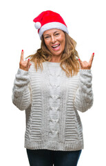 Middle age senior hispanic woman wearing christmas hat over isolated background shouting with crazy expression doing rock symbol with hands up. Music star. Heavy concept.