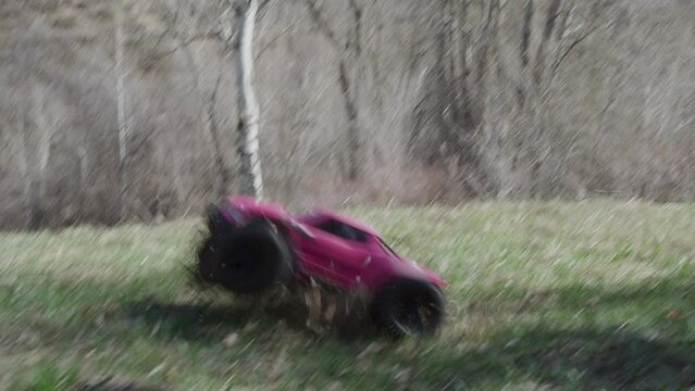Pink RC car driving off hill in forest - slow motion shot