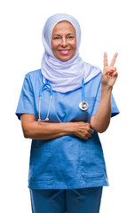 Middle age senior arab nurse woman wearing hijab over isolated background smiling with happy face winking at the camera doing victory sign. Number two.