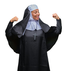 Middle age senior christian catholic nun woman over isolated background showing arms muscles...