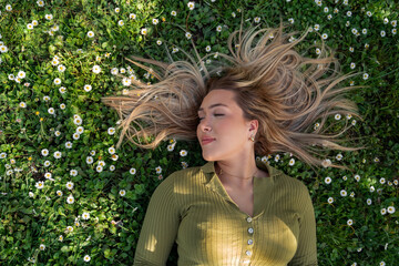 Beautiful blonde girl with beautiful long hair laying in the grass, spring time, beauty portrait. Hair model 