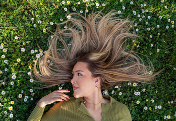 Beautiful blonde girl with beautiful long hair laying in the grass, spring time, beauty portrait
