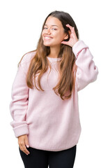 Obraz na płótnie Canvas Young beautiful brunette woman wearing pink winter sweater over isolated background smiling with hand over ear listening an hearing to rumor or gossip. Deafness concept.