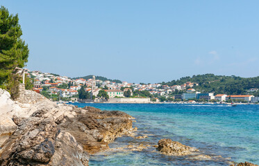 View from rugged rocky coastline across harbour to tourist and fishing township of Hvar - obrazy, fototapety, plakaty