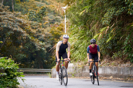 happy young asian couple cyclists riding bike outdoors on rural road