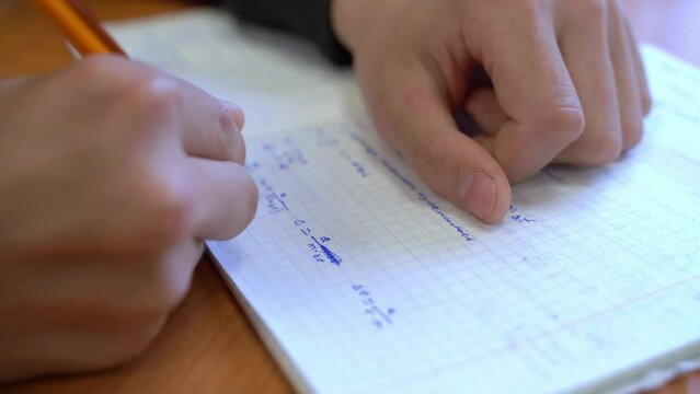 Close-up of hand holding pen, solving mathematical equations, writing formulas on checkered notebook in class at school Exam, physics test, student quickly and decisively writes the answer Math Tutor
