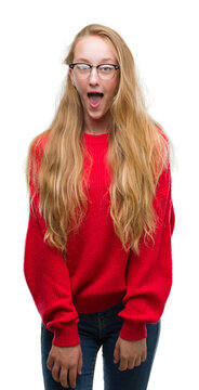 Blonde teenager woman wearing red sweater afraid and shocked with surprise expression, fear and excited face.