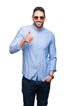 Fototapeta Young handsome man wearing sunglasses over isolated background doing happy thumbs up gesture with hand. Approving expression looking at the camera with showing success.