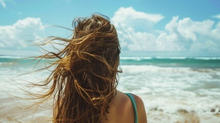 A woman gazes out at the expansive ocean horizon long hair blowing in the salty sea breeze as stands on the sandy beach. . . - obrazy, fototapety, plakaty