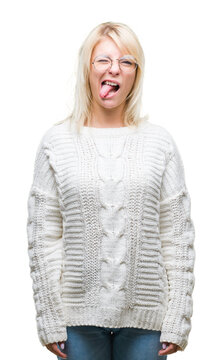 Young beautiful blonde woman wearing winter sweater and glasses over isolated background sticking tongue out happy with funny expression. Emotion concept.